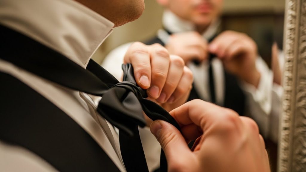 Luxury Black Tie Men’s Wedding Style: Timeless Groom Inspiration 4 Groom tying black silk bow tie in front of mirror.